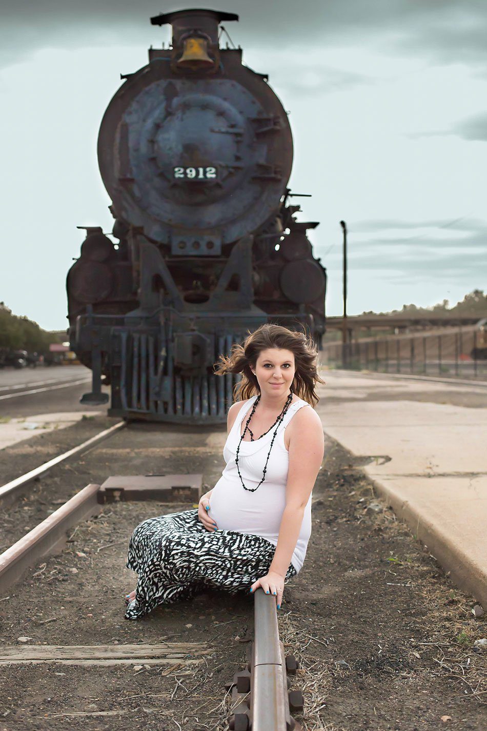 Pregnant mom sits on the train tracks in front of the engine at Pueblo railroad museum. Photo by Pueblo maternity photographer.