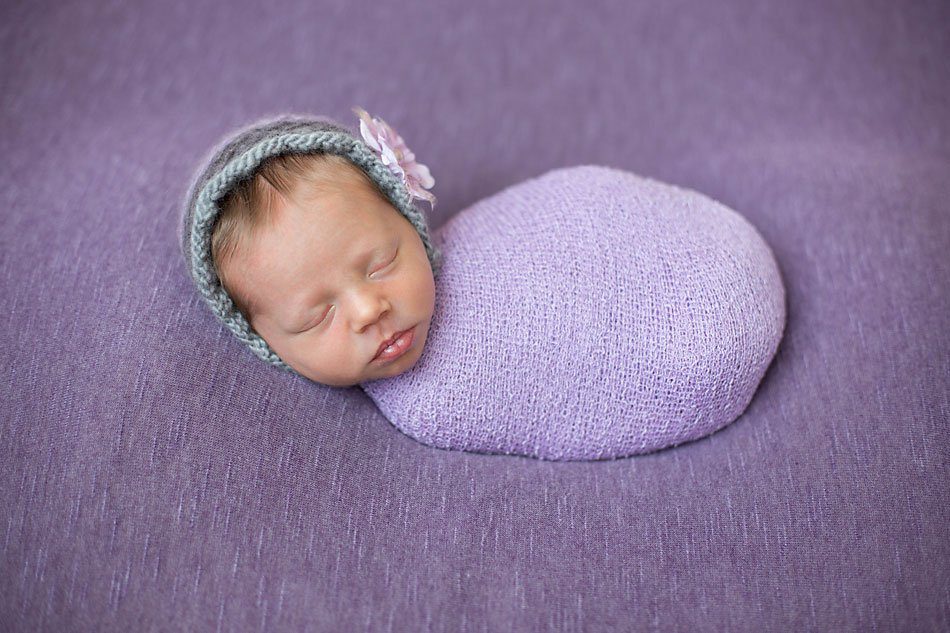 Newborn girl wrapped in purple sleeps on a purple blanket while being photographed by Pueblo newborn photographer.