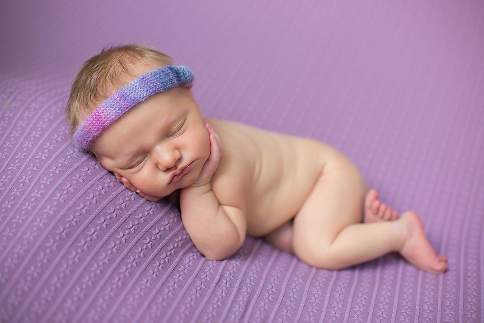 Newborn girl wearing a purple and pink headband sleeps on her side while being photographed by Pueblo newborn photographer.