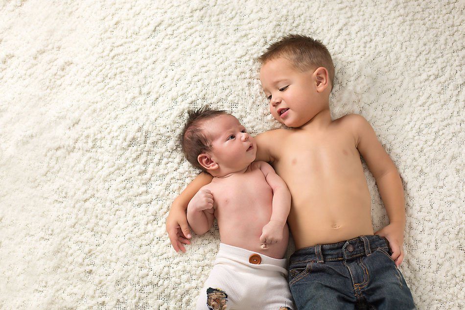 Newborn baby and his big brother lay on the floor and look at each other. Newborn photos by Pueblo newborn photographer K.D. Elise Photography.