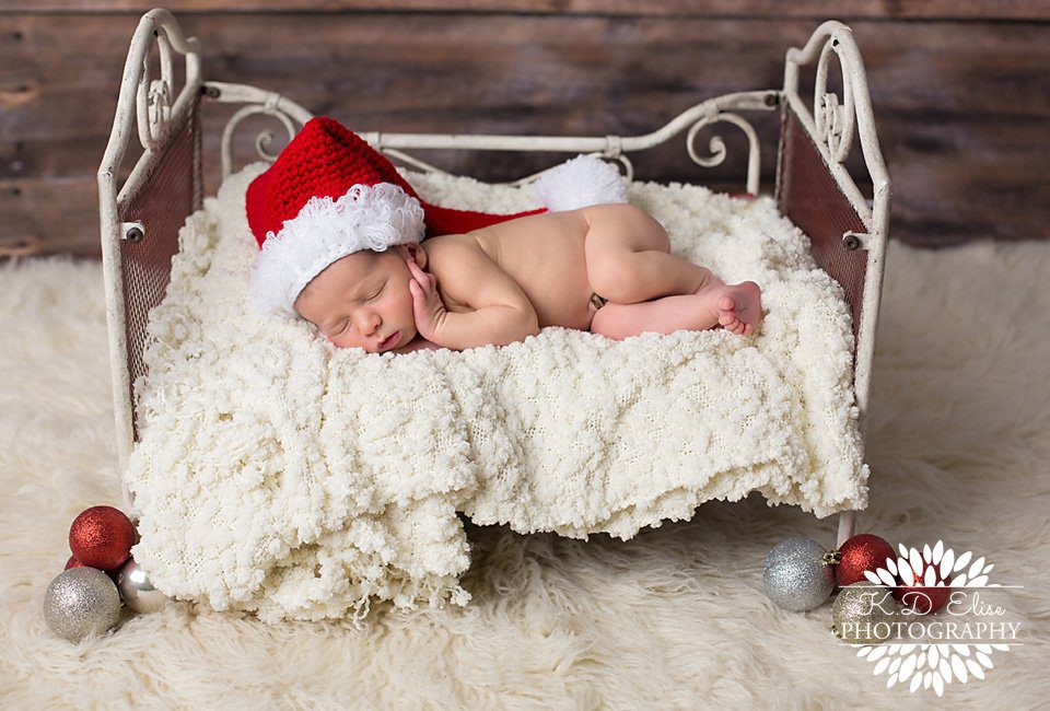 Sleeping newborn boy in a Santa hat, poses for his Christmas photos by Pueblo Newborn Photographer K.D. Elise Photography.