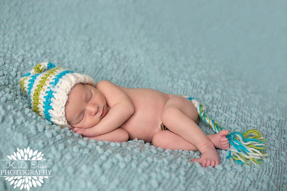 Newborn boy in green and white striped hat sleeps on a blue blanket. Newborn photography by Pueblo CO photographer K.D. Elise Photography.