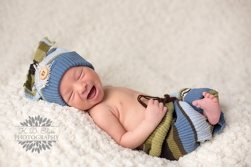 Sleeping baby boy in striped outfit grins at the camera. Newborn photography by Pueblo CO photographer K.D. Elise Photography.