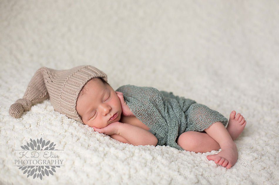 Baby boy wrapped in green and wearing a tan pixie hat sleeps on a cream blanket. Newborn photography by Pueblo CO newborn photographer K.D. Elise Photography.