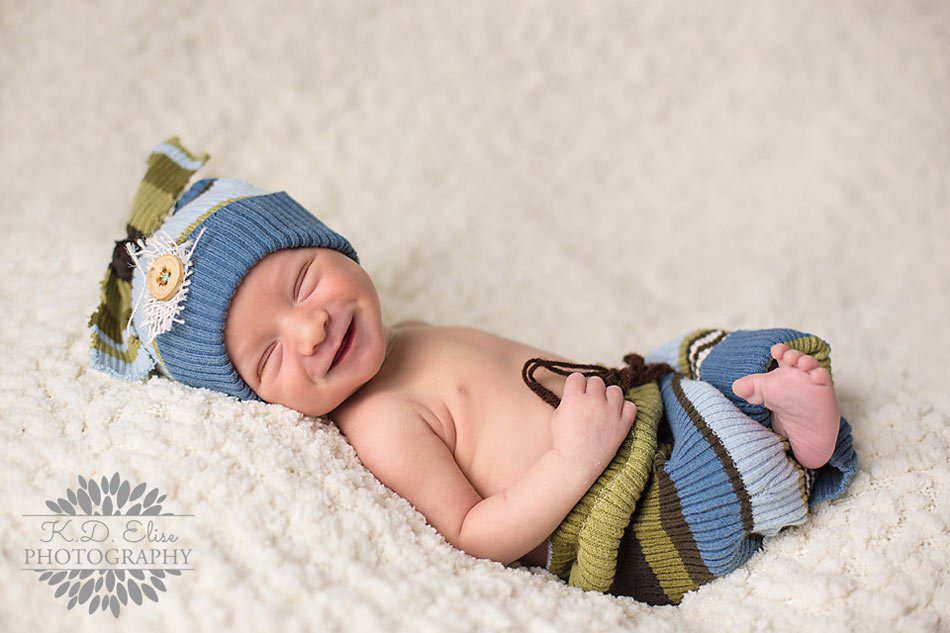 Sleeping baby boy smiles at the camera during his newborn photography session with Pueblo CO newborn photographer.