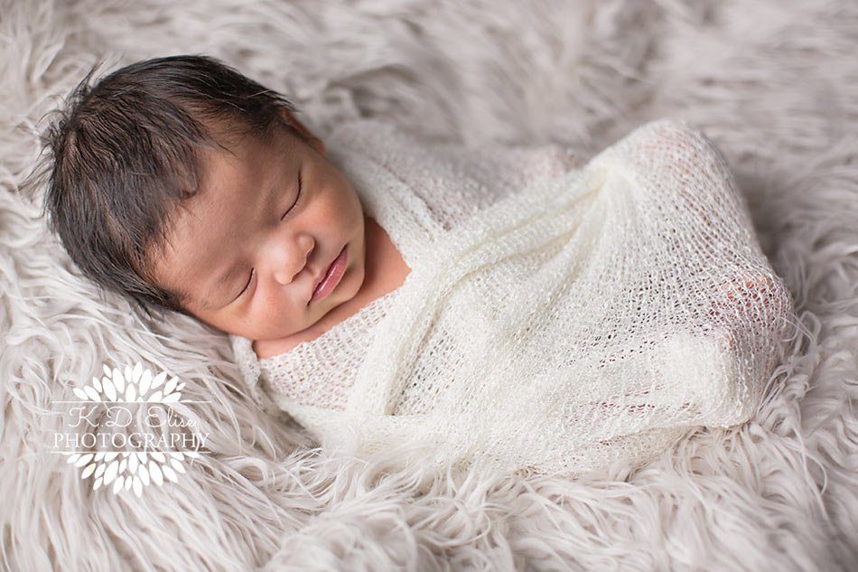 Baby boy wrapped in white, laying on a white fur by Pueblo newborn photographer K.D. Elise Photography