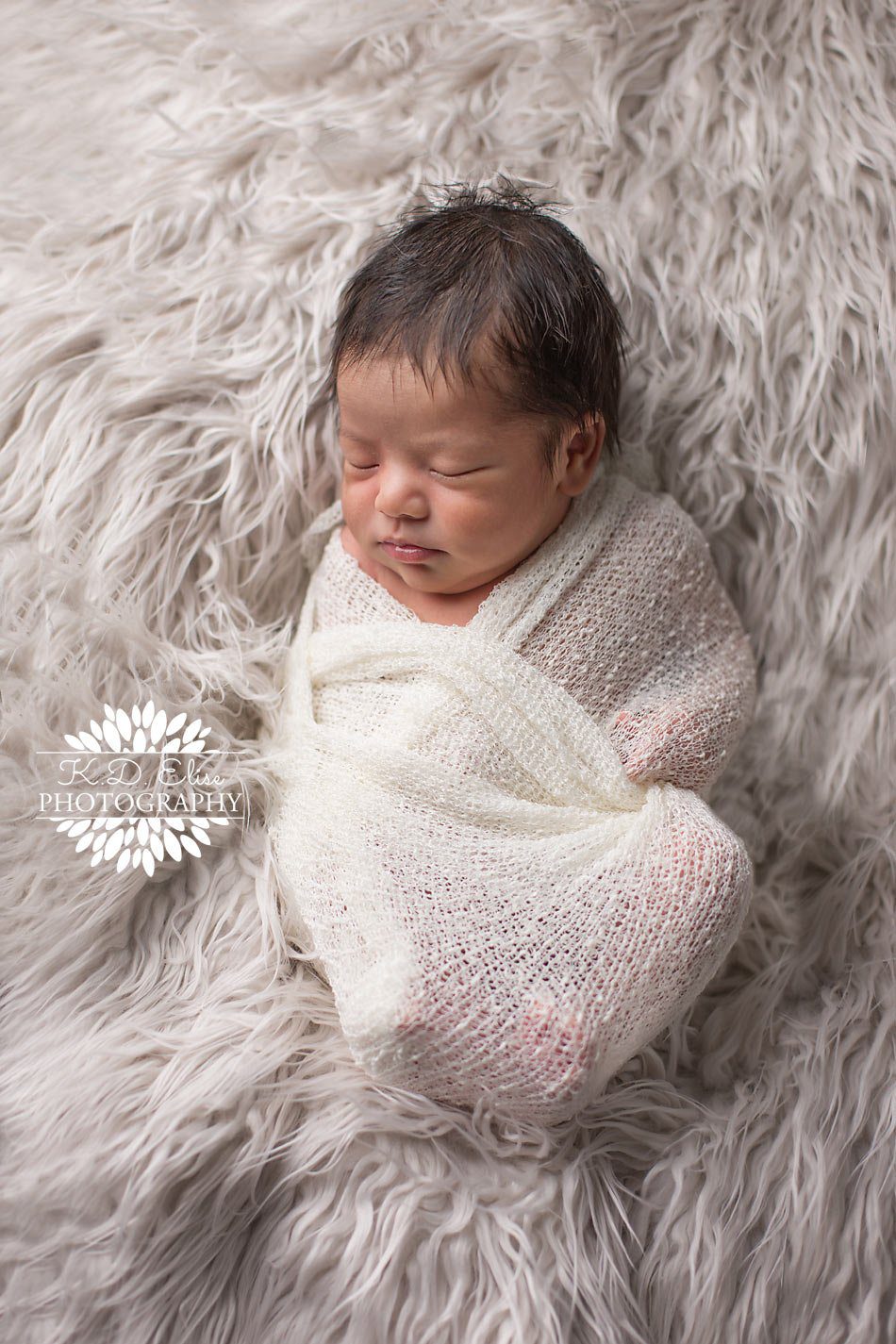 Newborn photography, baby boy wrapped up in a white wrap sleeping on a white fur rug. By Pueblo newborn photographer K.D. Elise Photography