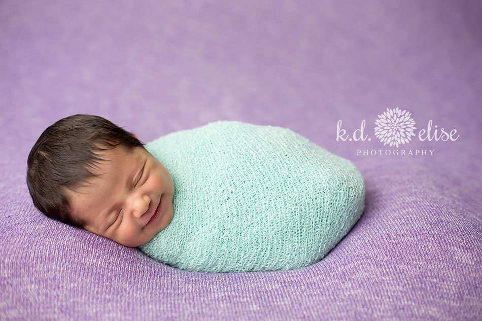 Baby girl in purple and green smiling in her sleep by Colorado Springs newborn photographer K.D. Elise Photography.