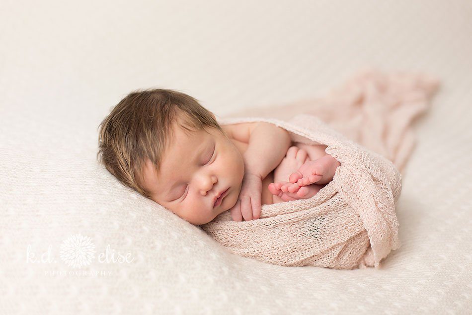 Newborn girl, curled up in a pink wrap and sleeping peacefully. Newborn portrait by K.D. Elise Photography.