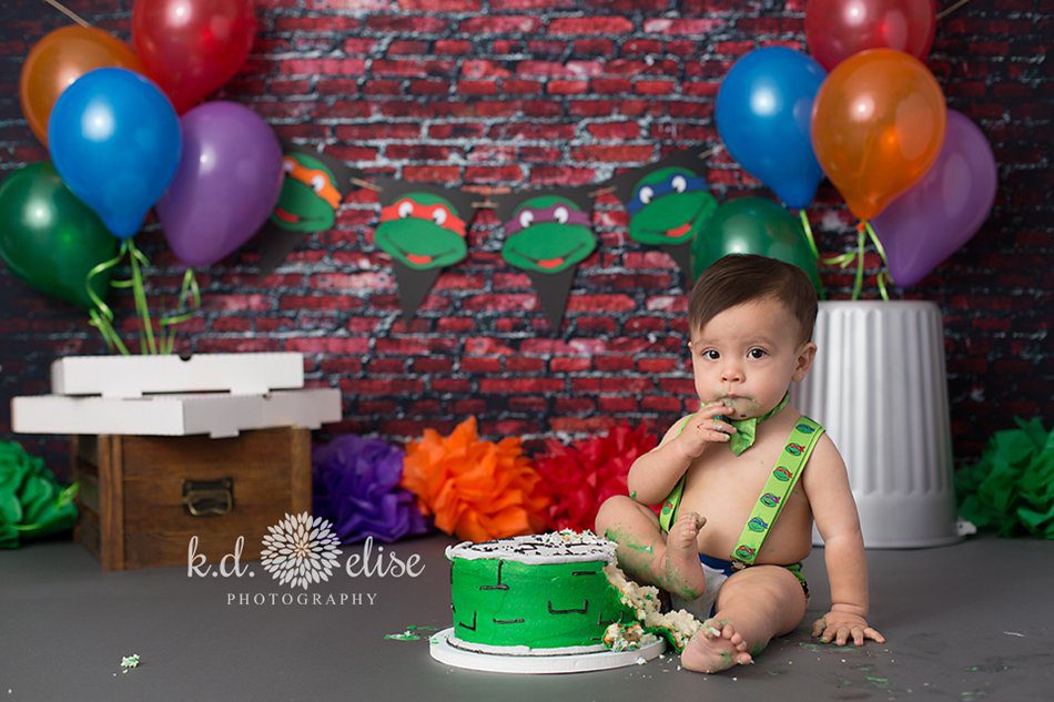 One year old boy eating cake during Teenage Mutant Ninja Turtle themed cake smash.