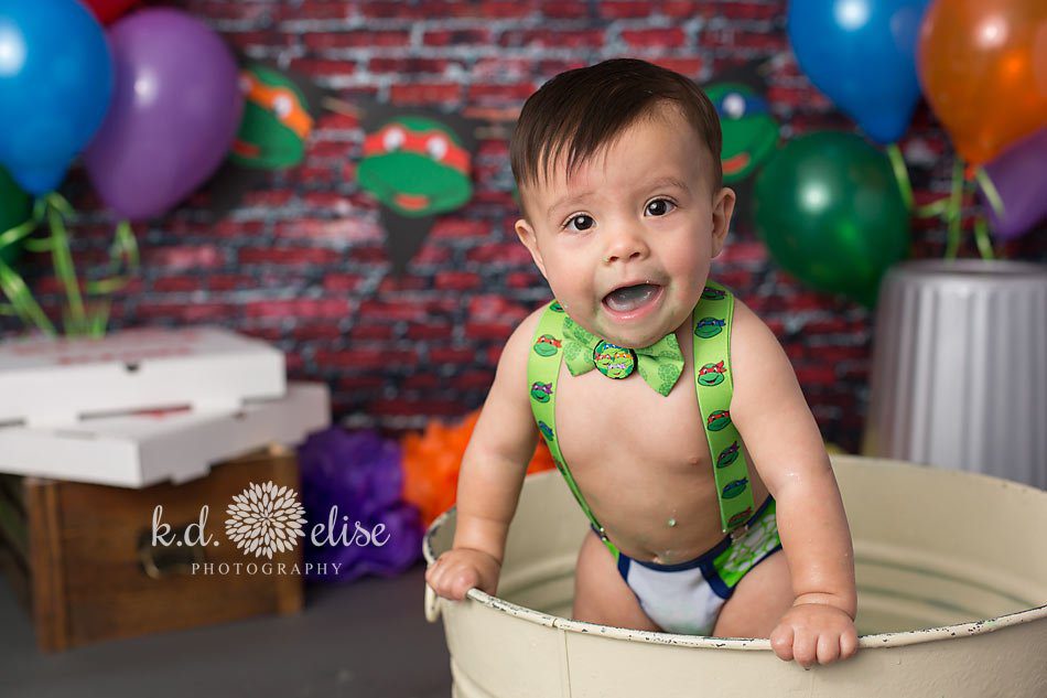 Smiling baby boy leaning over edge of metal wash basin.