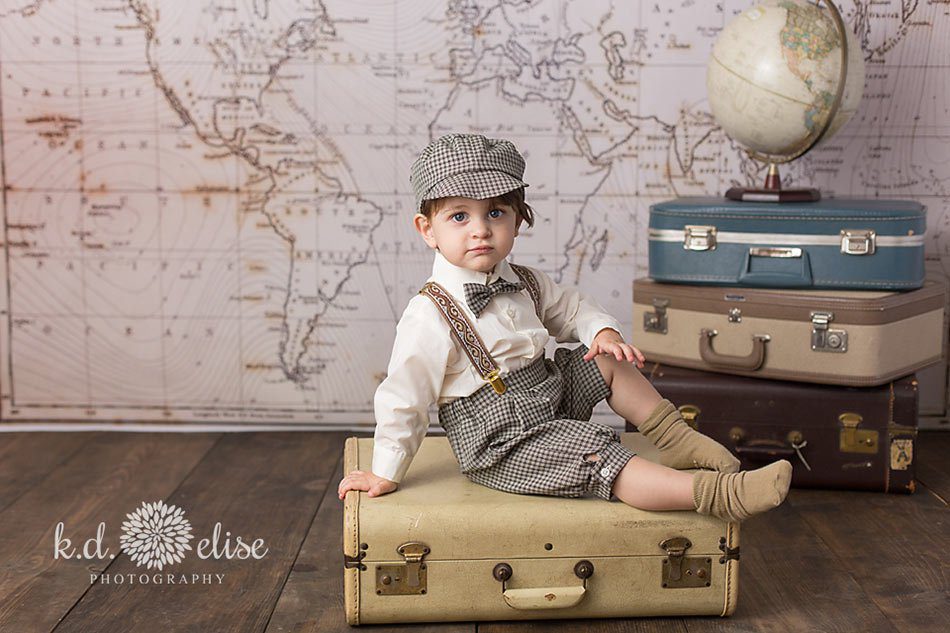 One year old boy sitting on vintage suitcases during themed children's photoshoot with K.D. Elise Photography.