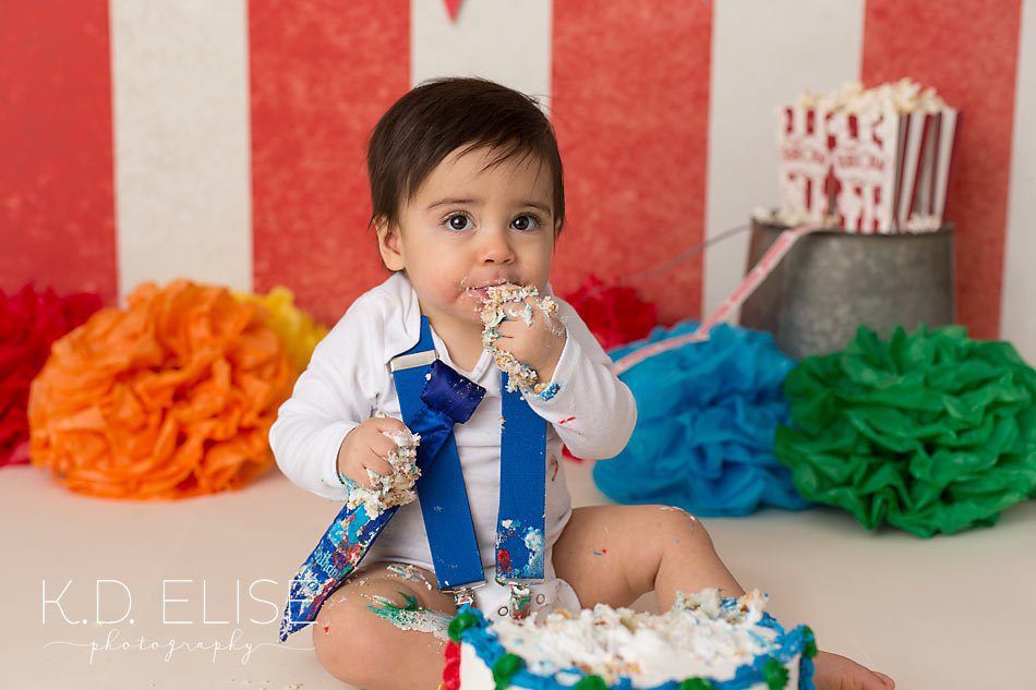 Baby boy taking a bite of birthday cake during his first birthday photos with K.D. Elise Photography.