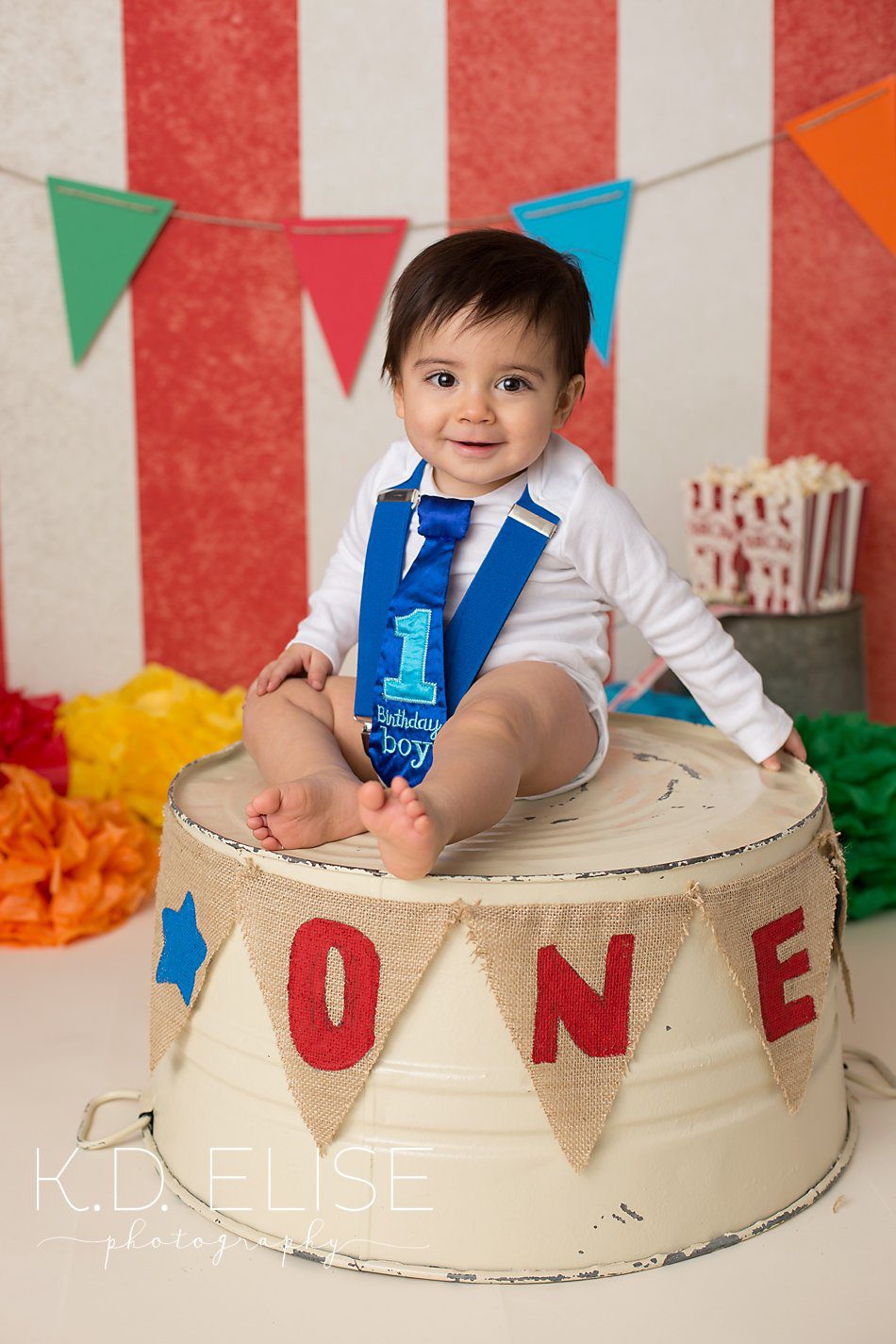 Circus themed first birthday photos of little boy in blue suspenders and tie sitting on ring master's podium.
