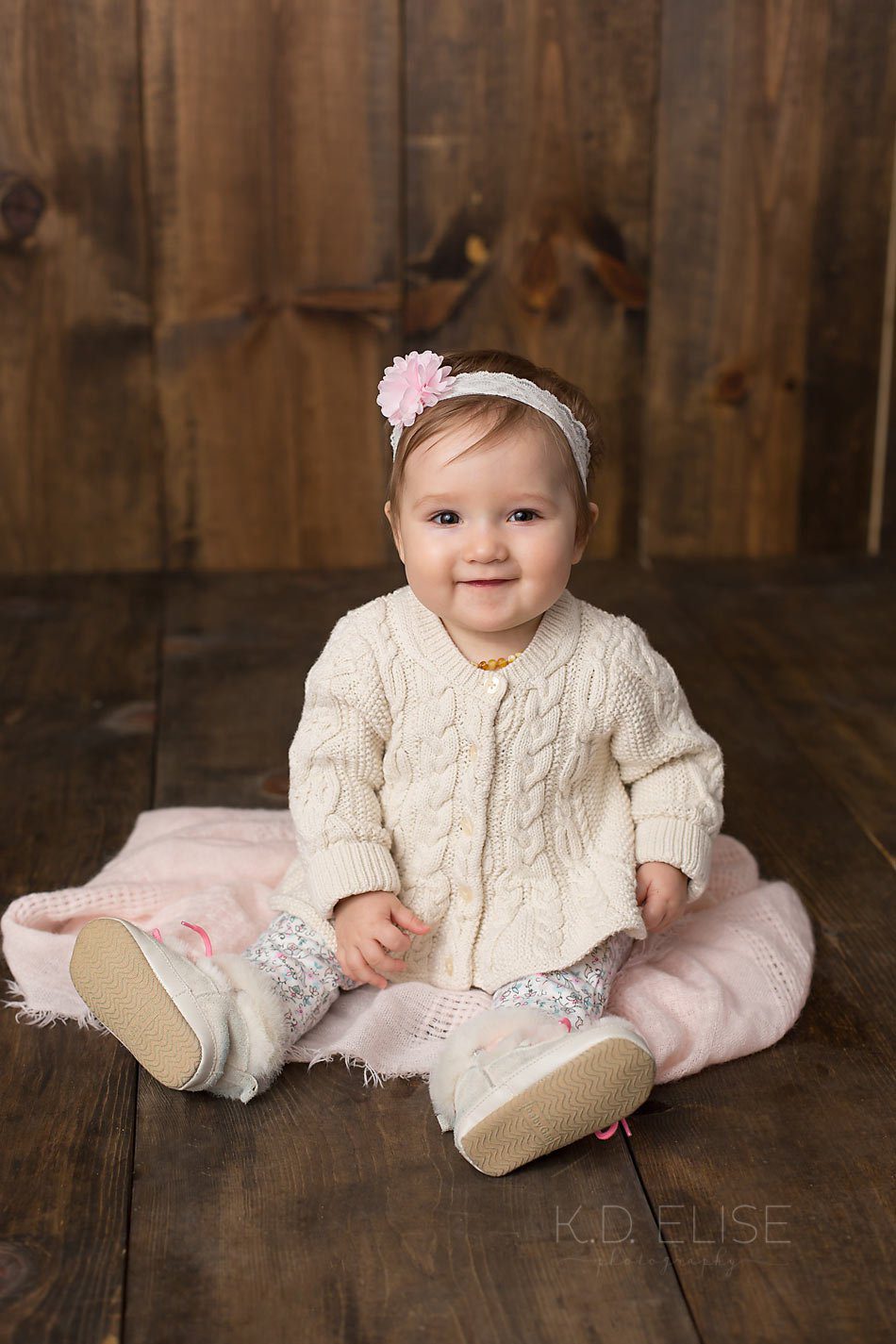 Baby girl in cream and pink smiles at the camera. Colorado Springs baby photography by K.D. Elise.