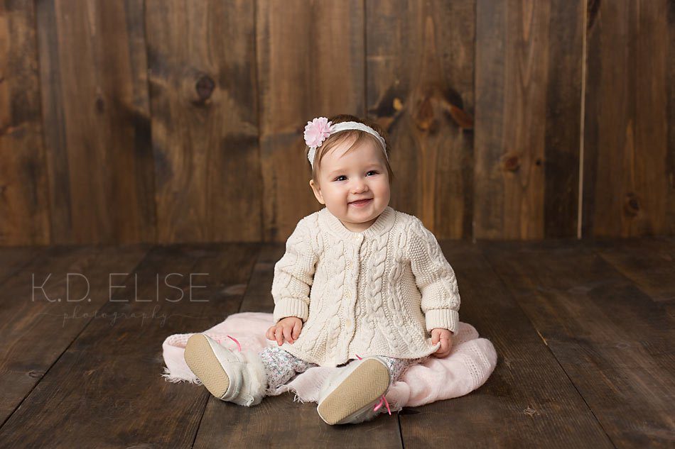 Baby girl in cream and pink outfit on wood floor backdrop by Colorado Springs baby photographer K.D. Elise Photography.