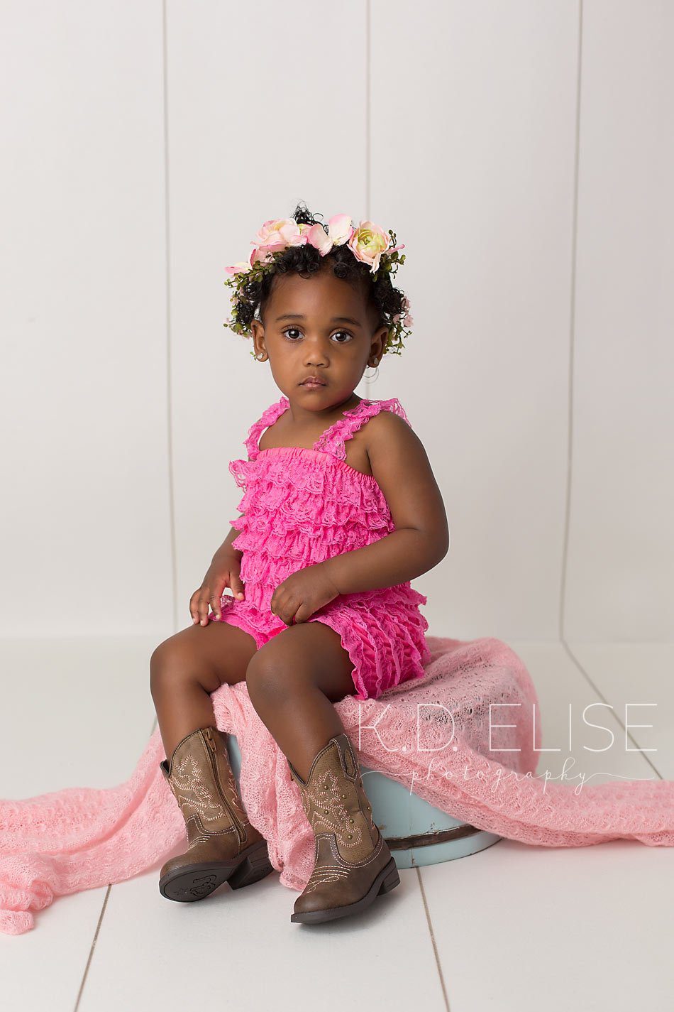 Little girl in pink romper sitting on a blue antique style bucket. By Pueblo children's photographer K.D. Elise Photography.