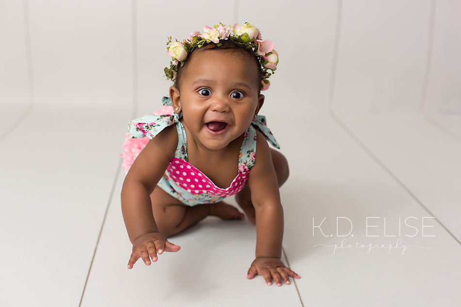 Baby girl in blue romper crawling on a white wood floor during photography session with Pueblo Children's photographer K.D. Elise Photography.
