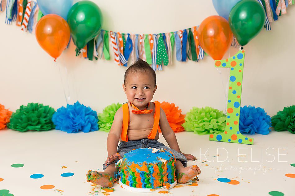 Cake smash photo of little boy with orange, blue and green setup. First birthday photos by Pueblo photographer K.D. Elise Photography.