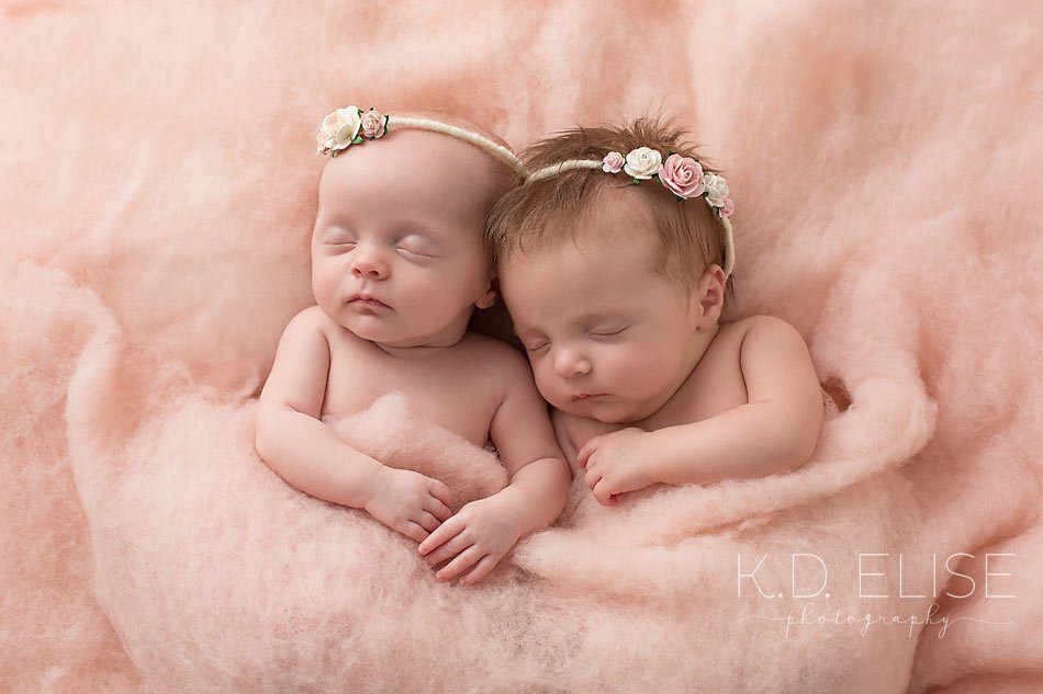 Newborn twin girls wearing floral crowns lay in fluffy pink wool. Twin newborn portraits by Colorado Springs newborn photographer K.D. Elise Photography.