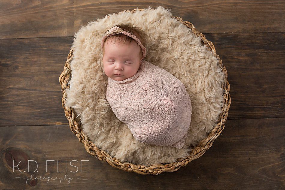 Newborn baby girl wrapped in pink in a basket.