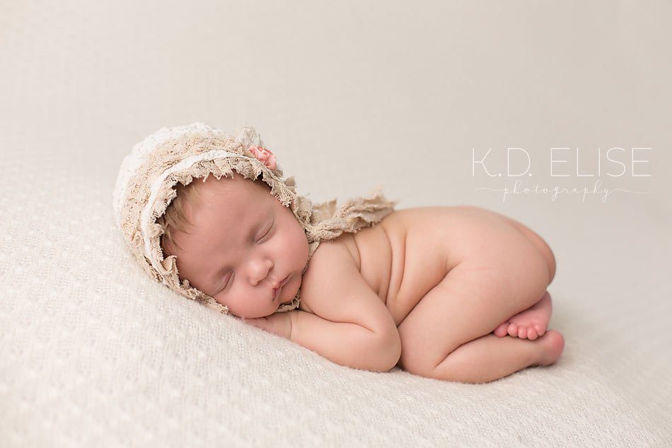 Baby girl in cream hat laying on her tummy. Newborn portrait by K.D. Elise Photography.