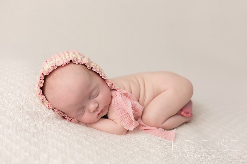 Baby girl in pink hat, laying on her tummy. Newborn photography by Colorado Springs newborn photographer K.D. Elise Photography.