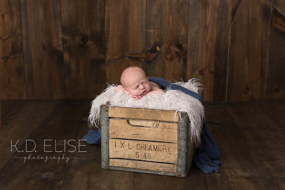 Newborn baby boy laying on fur in a vintage milk crate. Newborn portraits by Pueblo newborn photographer K.D. Elise Photography.