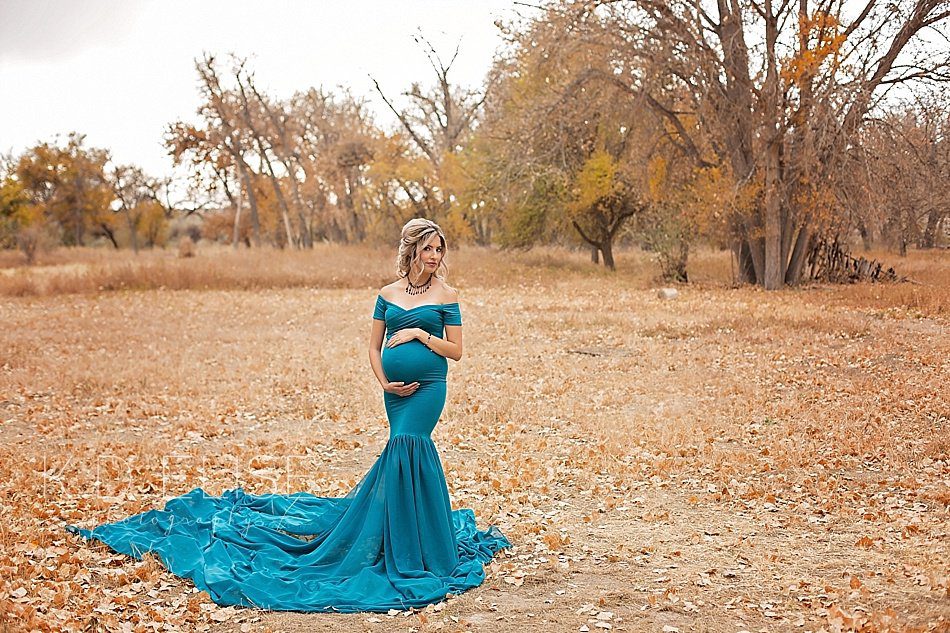 Maternity photo of mother to be in teal gown, standing in a field of fallen leaves.