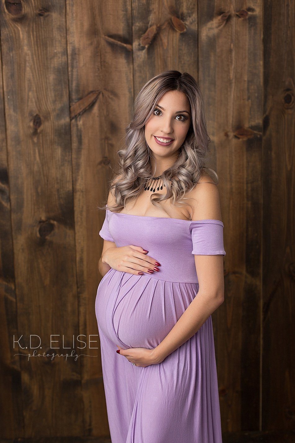Pregnant mom wearing lavender gown cradles her belly during maternity portraits with Pueblo maternity photographer K.D. Elise Photography.