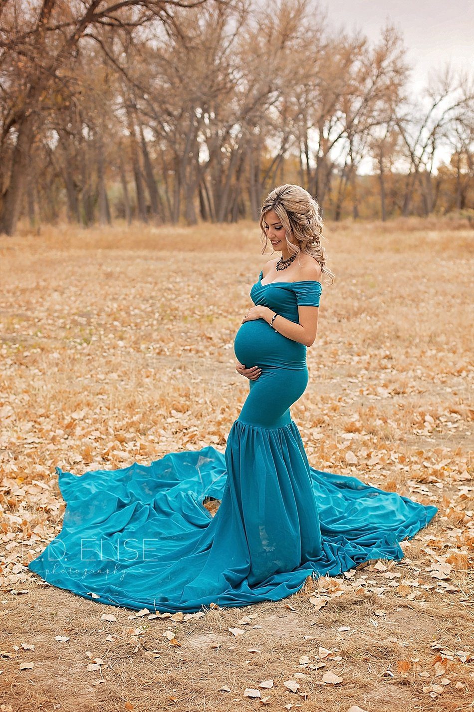 Pregnant mom in teal maternity gown looking down at her belly during maternity portraits with Pueblo maternity photographer K.D. Elise Photography.