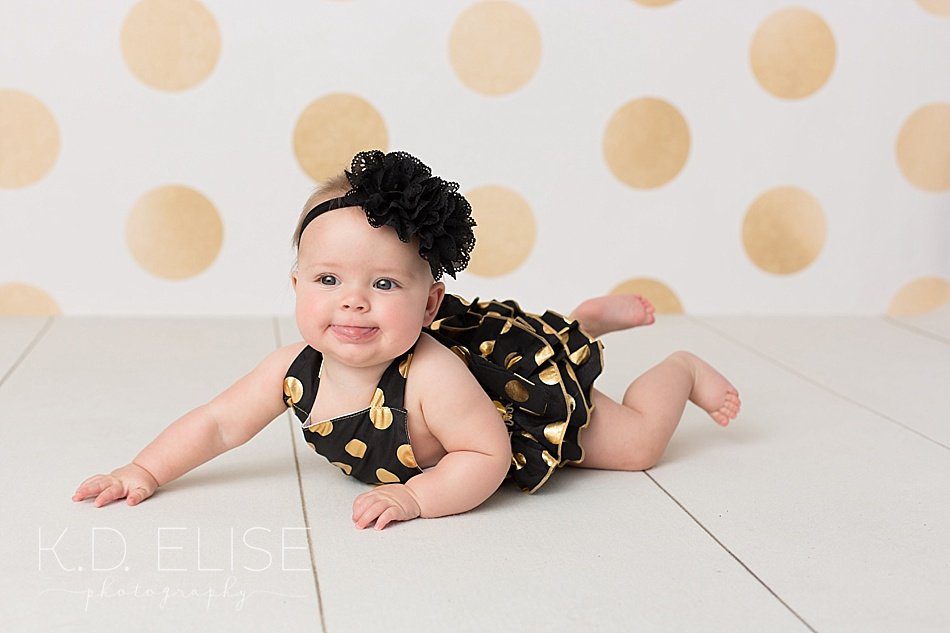 Baby girl in black and gold romper sitting up by Colorado Springs baby photographer K.D. Elise Photography.
