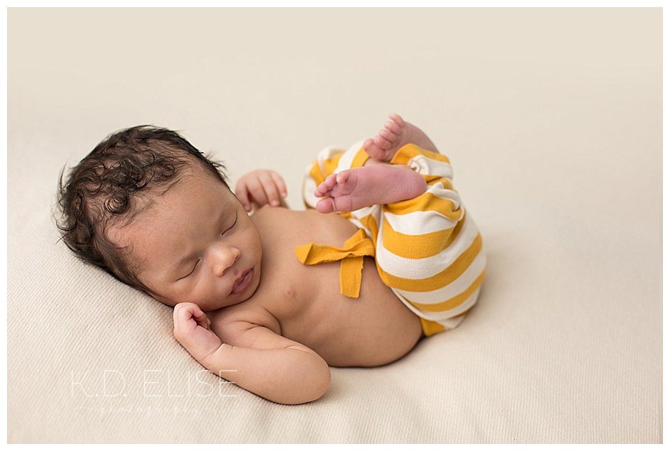 Baby boy in yellow and cream striped pants, laying on his back with his legs curled up. Newborn portraits by Pueblo and Colorado Springs newborn photographer K.D. Elise Photography.