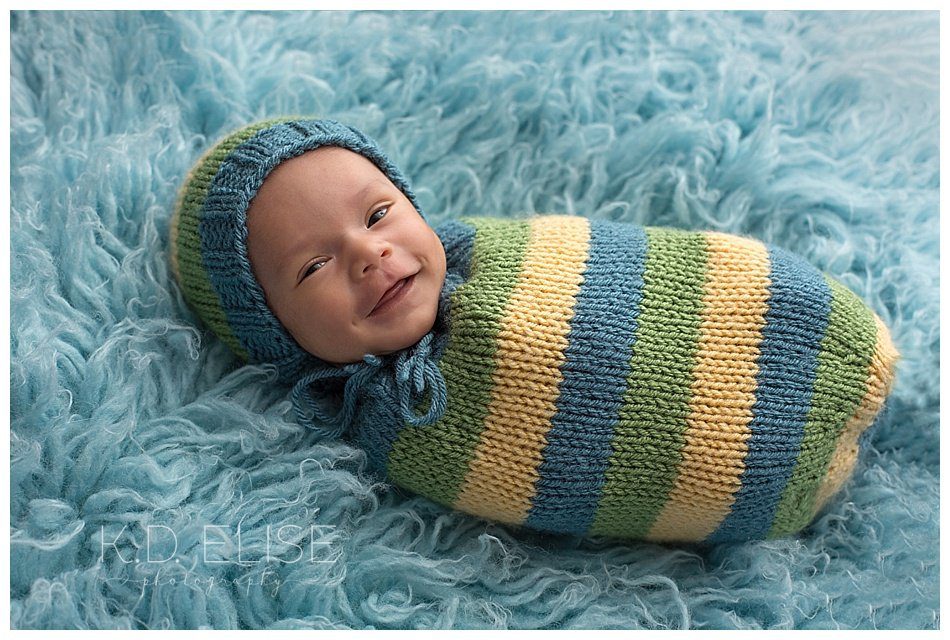Newborn baby boy smiles at the camera during newborn portrait session with Colorado springs and Pueblo newborn photographer K.D. Elise Photography.