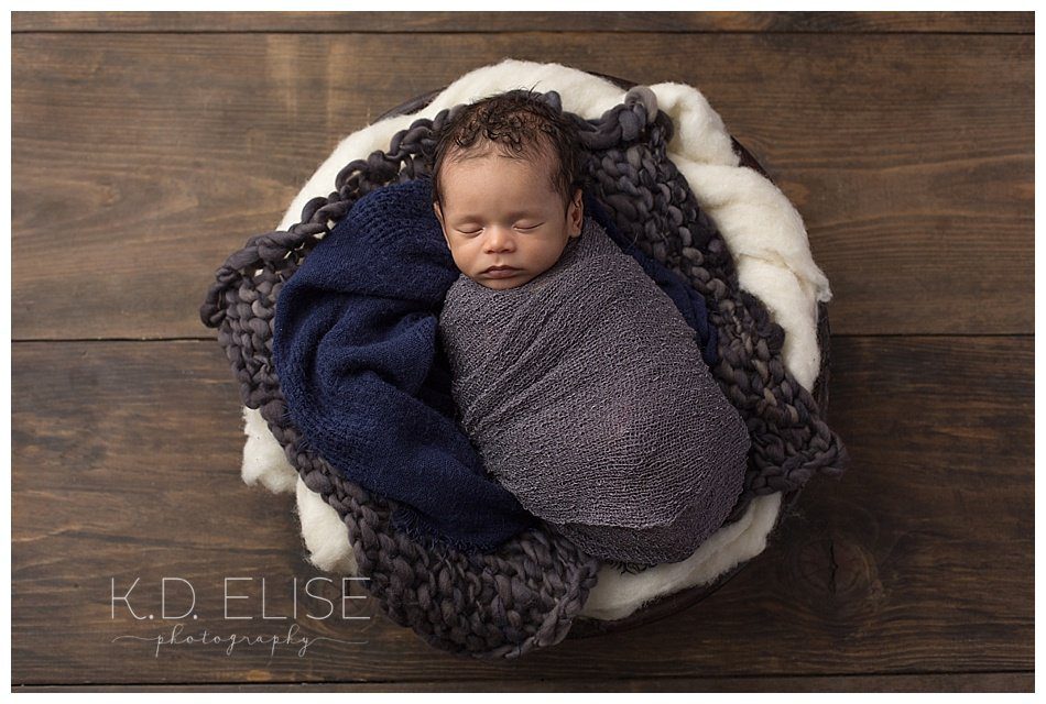 Newborn boy laying in a bowl surrounded by blue and cream. Newborn portraits by K.D. Elise Photography.