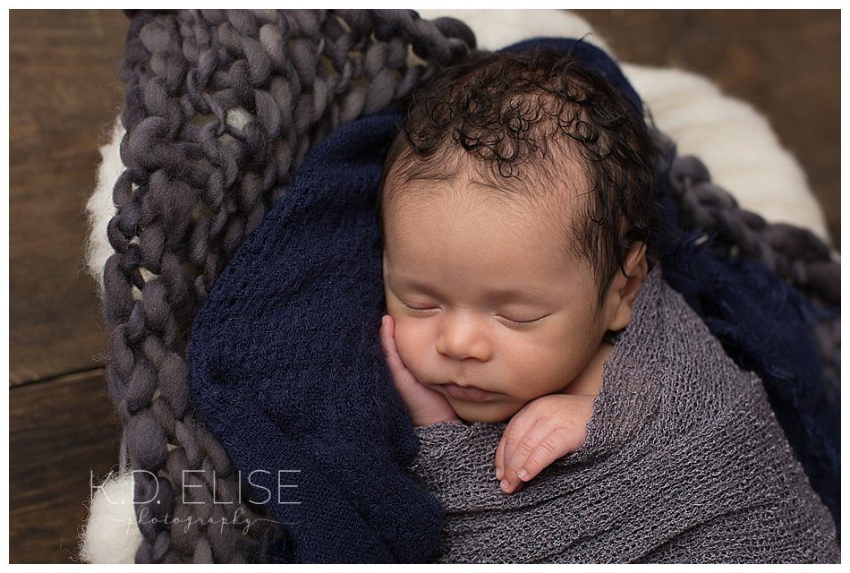 Close up of newborn baby boy laying on grey and blue fabric. Newborn portraits by Pueblo photographer K.D. Elise Photography.