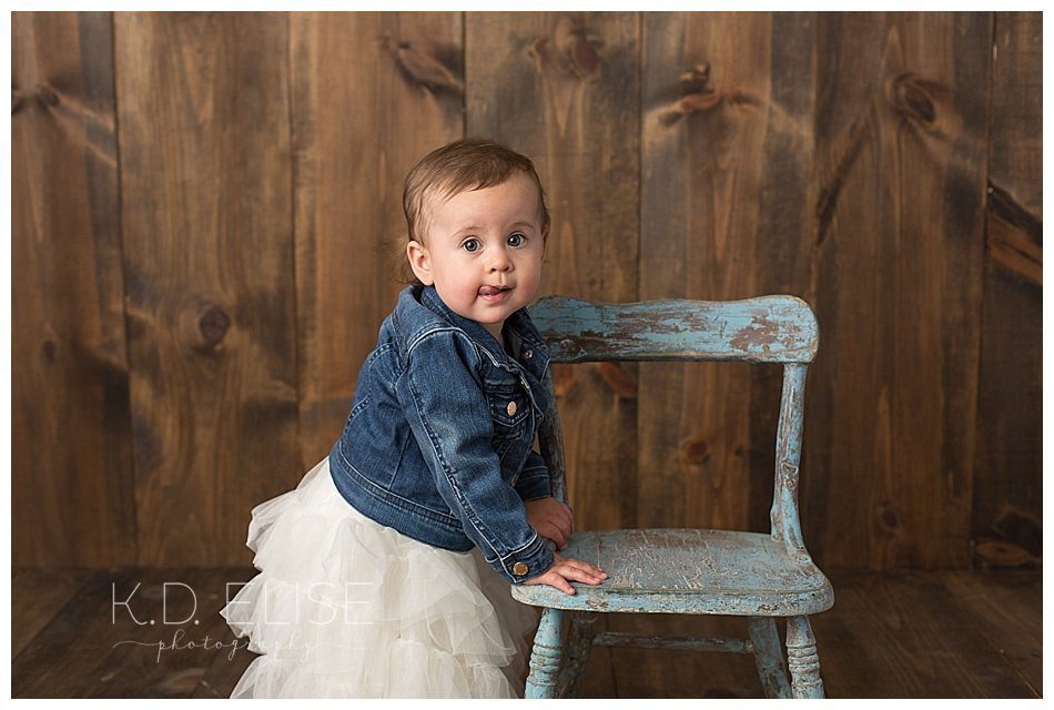 One year old girl standing next to a chair during her first birthday photos with Pueblo photographer K.D. Elise Photography.