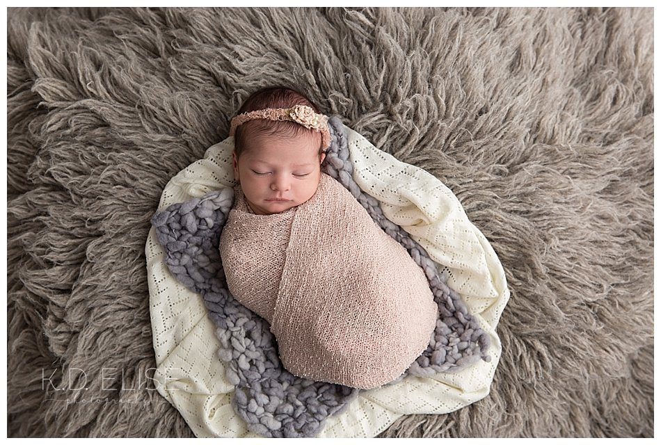 Newborn baby photos of baby girl wrapped in pink lying on layers of grey fur by Colorado Springs newborn photographer K.D. Elise Photography.
