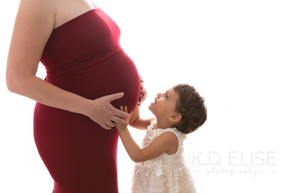 Little girl kissing her mom's belly during maternity photos with K.D. Elise Photography.