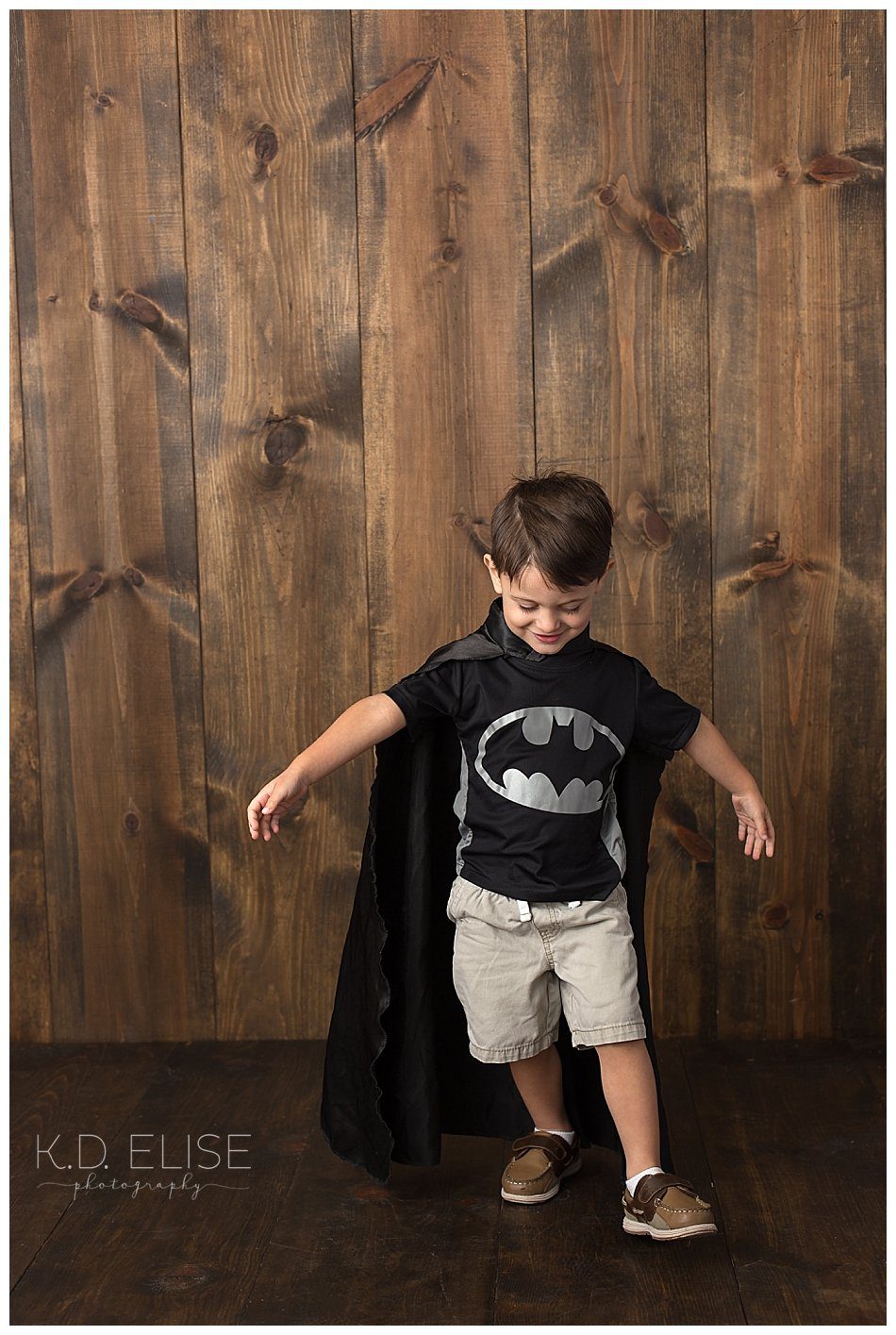 Little boy in batman shirt and cape during his third birthday portraits.