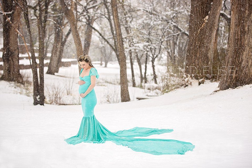 Pregnant mom in tiffany blue gown stands in the middle of a snowy forest during maternity session with Pueblo photographer K.D. Elise Photography.