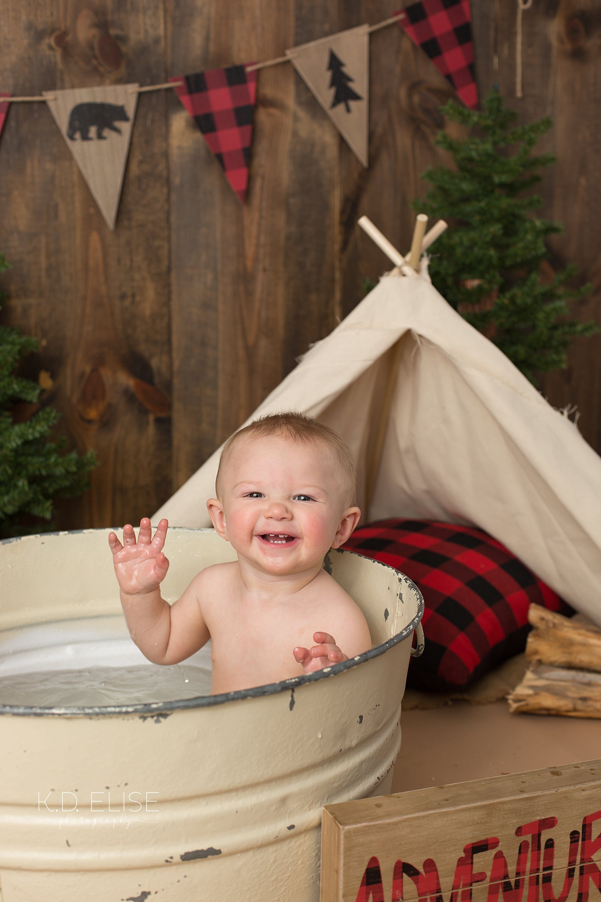 Smiling one year old boy playing in a metal wash basin after lumberjack themed cake smash with K.D. Elise Photography.