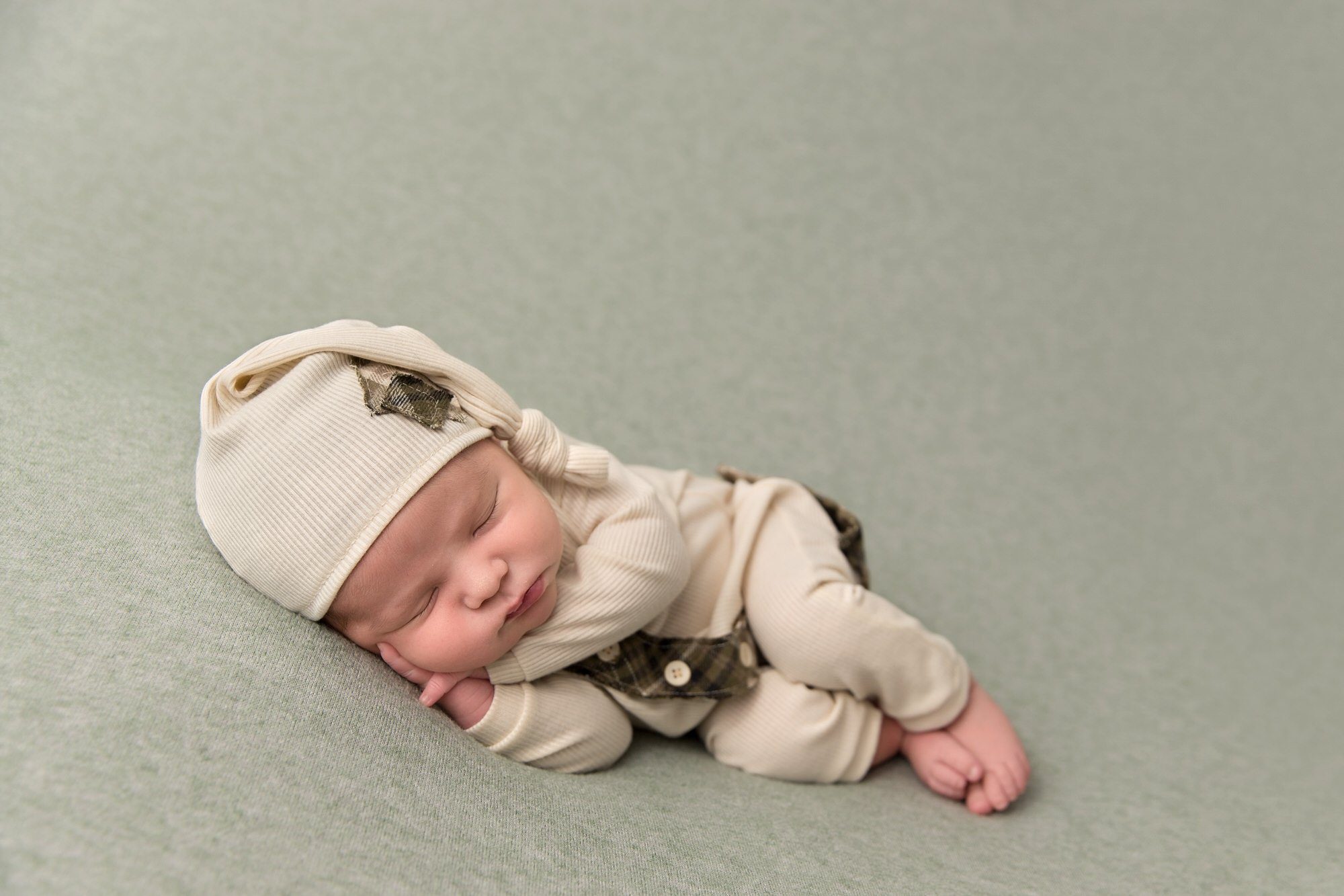 Newborn baby boy in sleepy cap and sleeper laying on his side. Photo by Pueblo Colorado Springs newborn photographer K.D. Elise Photography.
