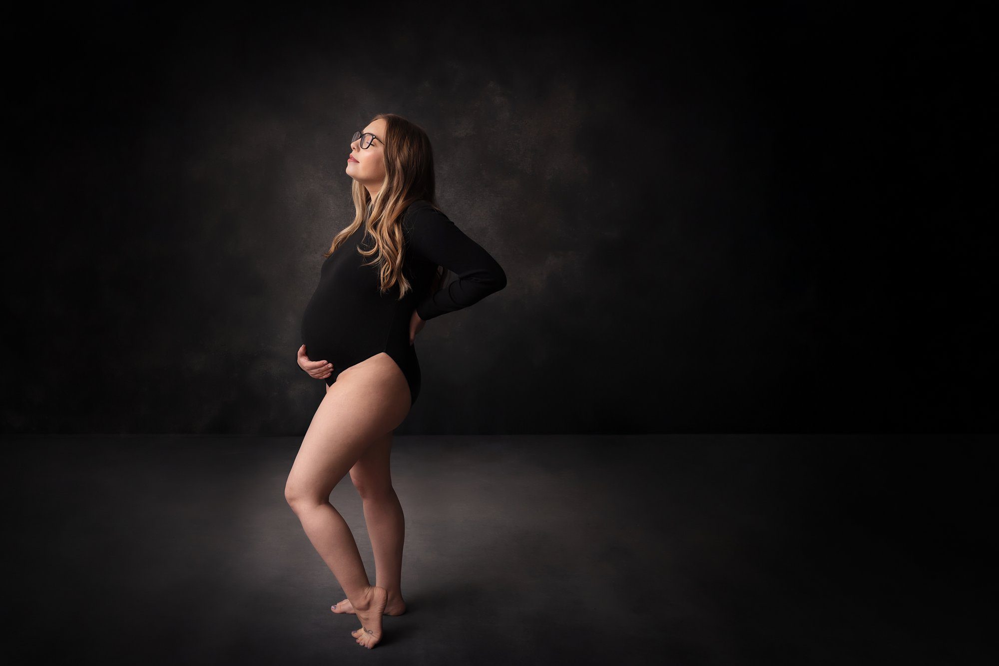 Pregnancy photo of mom in a black body suit, holding her stomach.