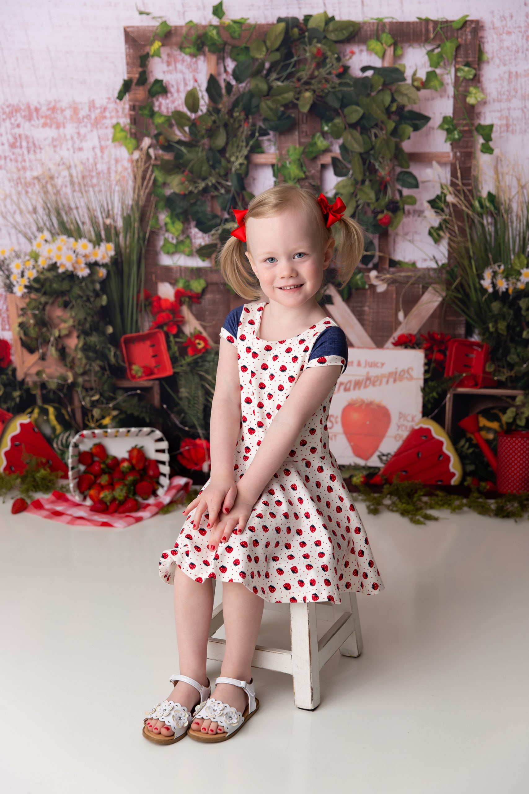 Girl in dress and pigtails on a bench. The backdrop is strawberries and watermelon.