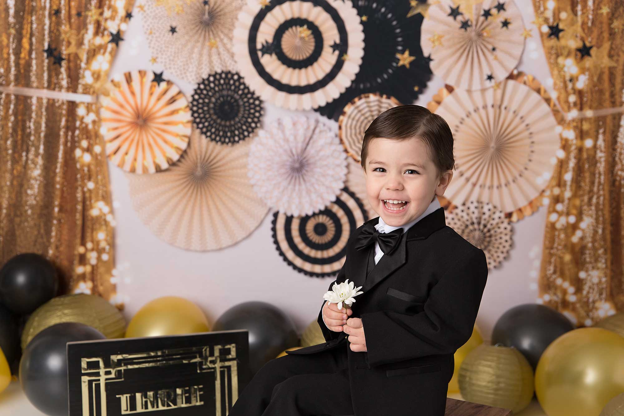 Smiling little boy sitting at a tiny piano in front of a Greater than Gatsby backdrop.