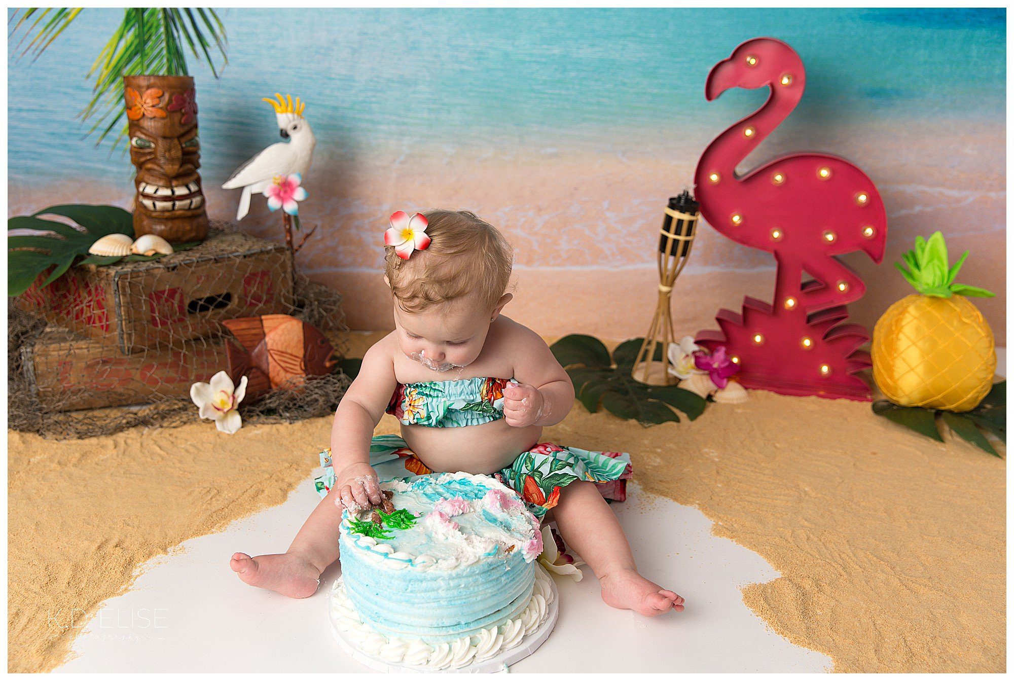 Baby girl eating cake during luau themed cake smash by Pueblo photographer K.D. Elise Photography. 