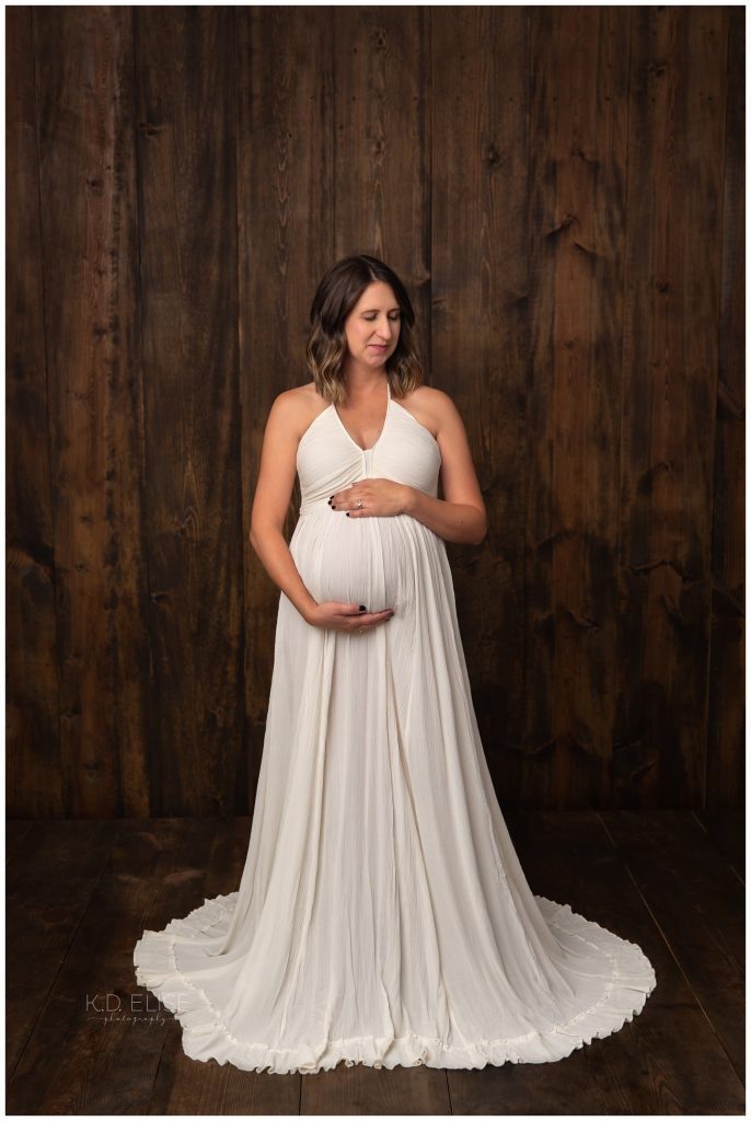 In studio maternity photography image of pregnant mom in a cream gown on wood backdrop.