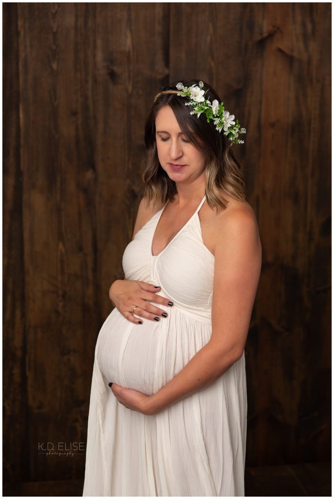 In studio maternity photo of pregnant mom in a cream gown, wearing a floral crown.