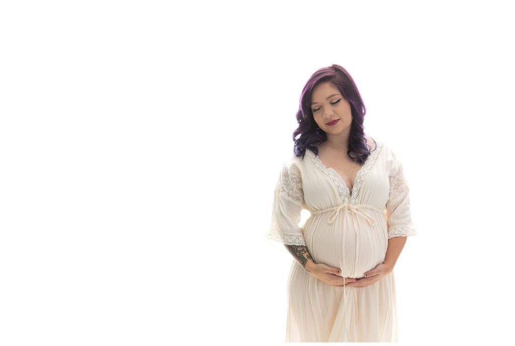 In studio maternity photo of pregnant mom in a cream gown, in front of a white background.